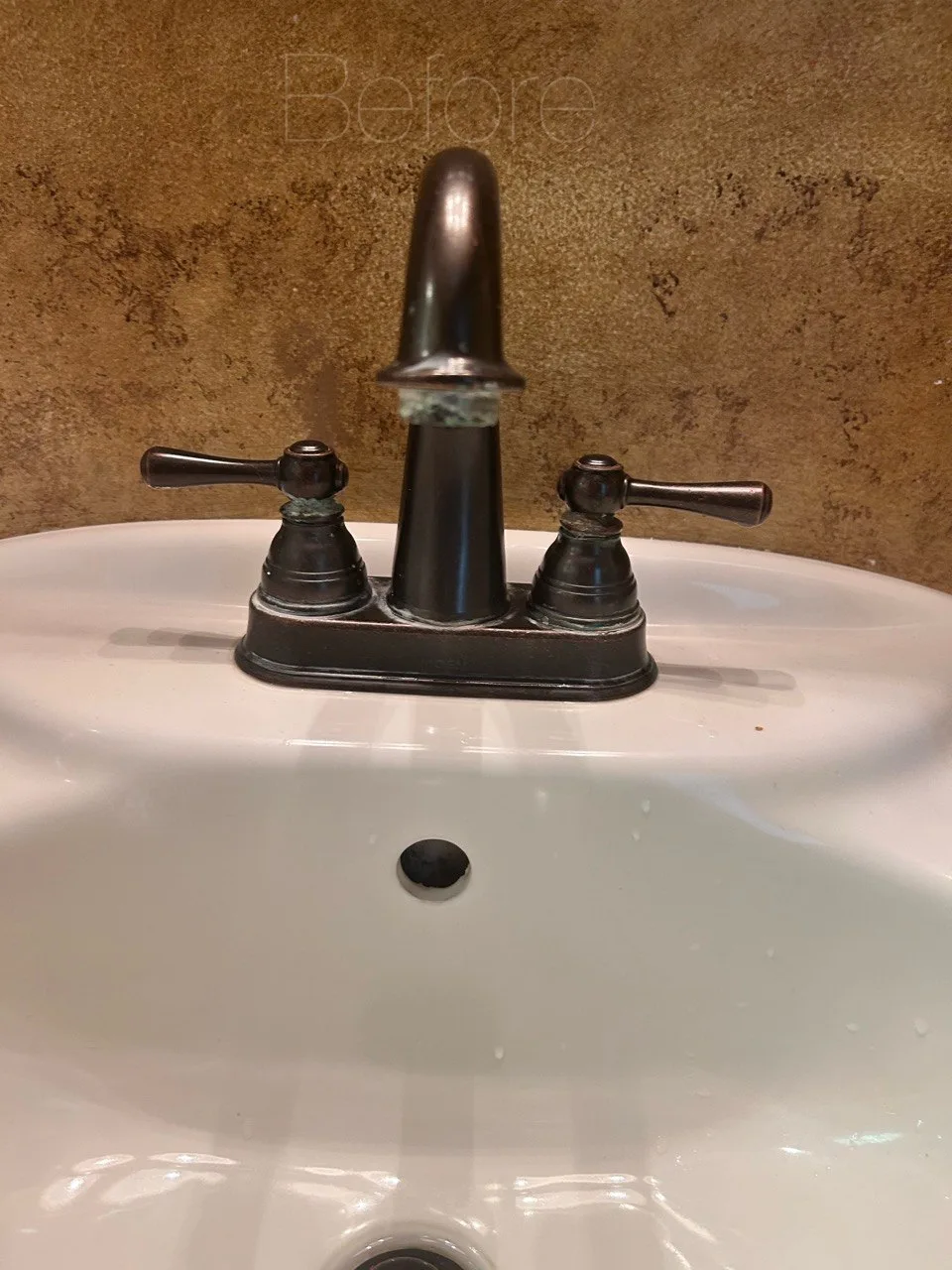Pale buildup around a bronze bathroom faucet and handles before cleaning