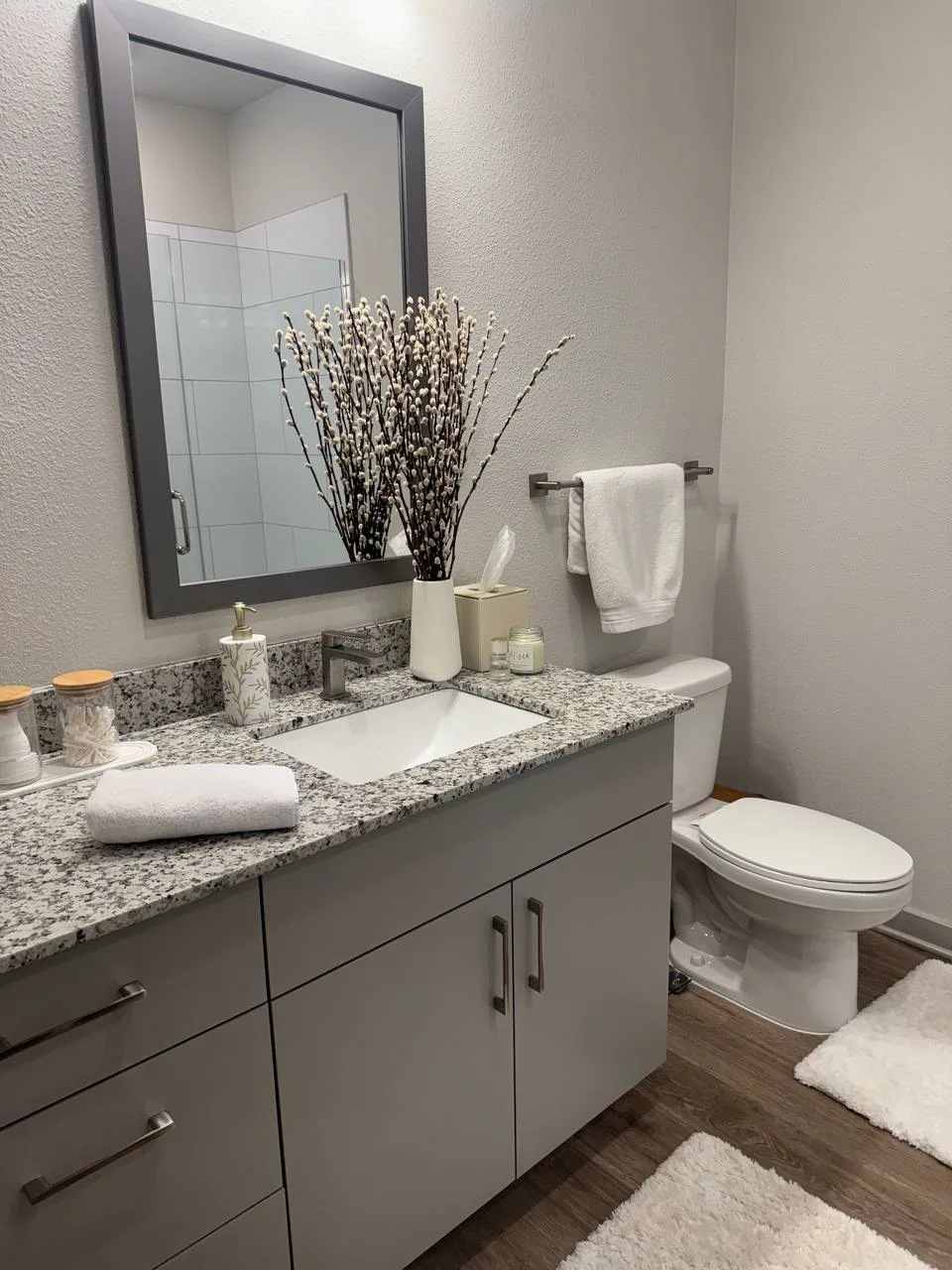 Clean bathroom with a gray vanity, granite countertop, mirror and folded white towels