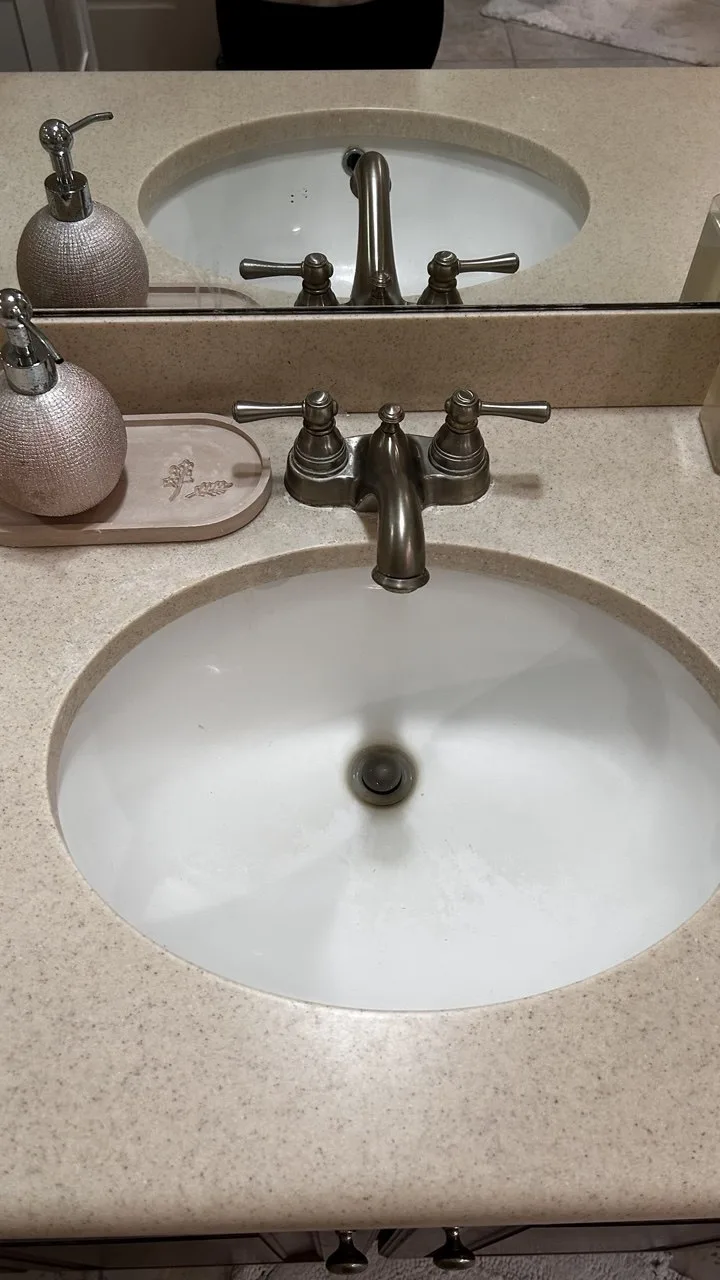 Marks around the drain and bowl of an oval bathroom sink before cleaning