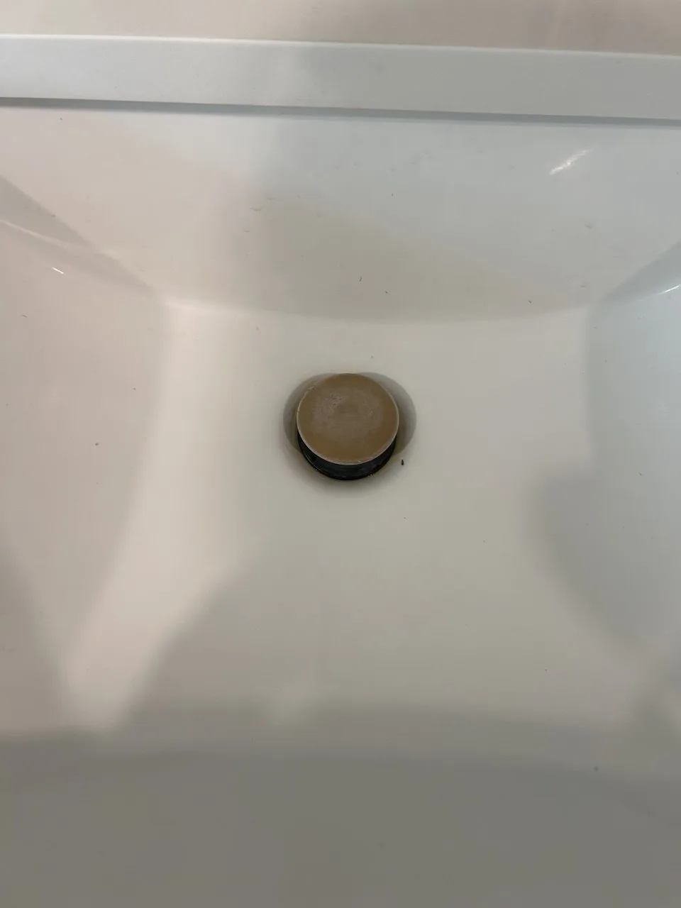 Close view of marks around the bronze drain stopper in a white sink before cleaning