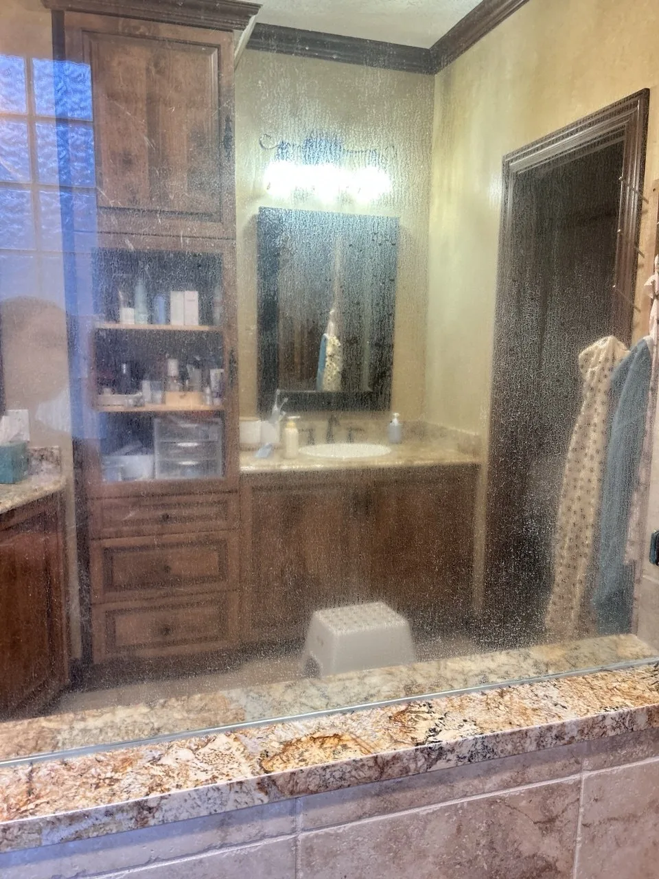 Residue on shower glass obscuring the wooden bathroom vanity before cleaning